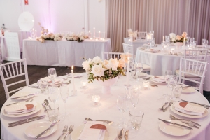 The Plympton Room is a large wedding function space at the Tradewinds Hotel. Here, round dining tables are laid with white tablecloth, a white rose centrepiece, and fine dining crockery.