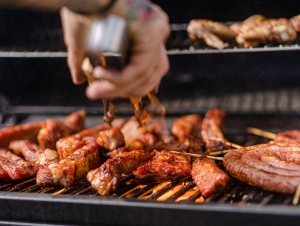 A chef grills ribs, sausages, and chicken wings on a barbecue
