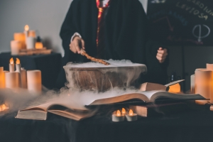 A wizard dressed in Hogwarts School of Witchcraft and Wizardry robes is doing some potion-making above a smoking cauldron
